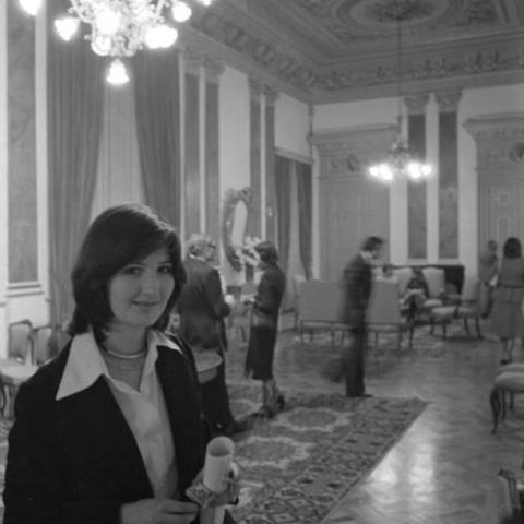 A woman holding a rolled program and a cigarette in theater lobby with ornate floor and ceiling