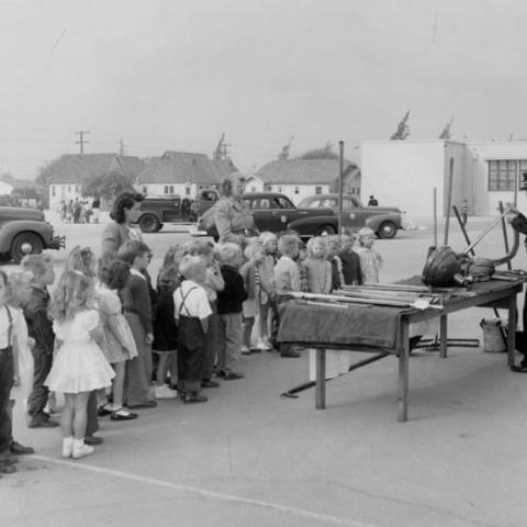 School children line up to watch a fire fighter demonstrate equipment during Fire Prevention week, Burbank, ca. 1950s, BUR03
