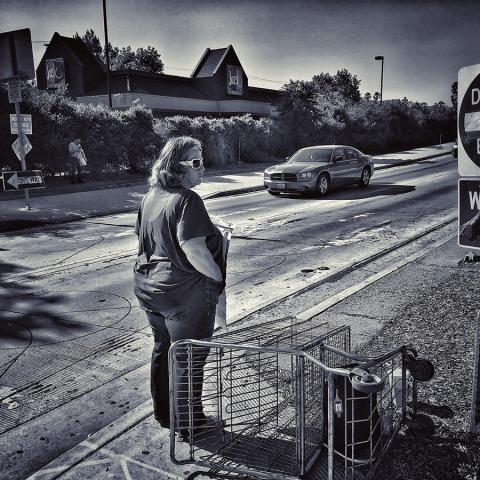 Kathy holding a sign at a freeway offramp next to traffic signs that read, “DO NOT ENTER” and “WRONG WAY”, ca. 1990.