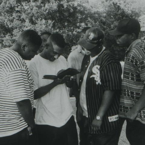 A group looks at photographs from an album while standing in the street. TBC.RCH