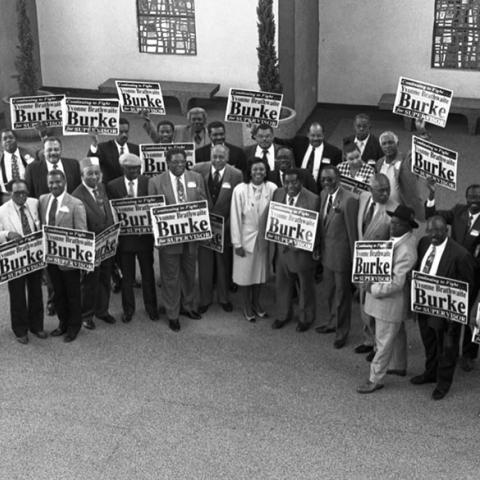 Group photograph of Yvonne Brathwaite Burke in a courtyard of the North Campus, West Angeles Church of God in Christ with a crowd holding signs reading, "Continuing to fight. Yvonne Brathwaite Burke for Supervisor." 1992. Digital ID: 11.06.GC.N35.B5.46.146.27