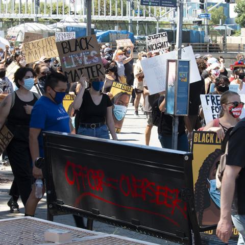Graffiti on the back of a bus bench reads "Officer = Overseer" at the "Farce of July" demonstration, organized by Black Lives Matter and local Indigenous groups. Olvera Street, 2020, KRT.D.B1.18.3563 