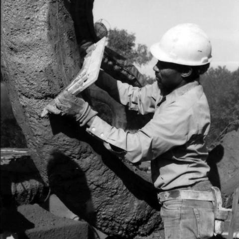 Member of crew using a guide to maintain uniformity of sculpture dimensions