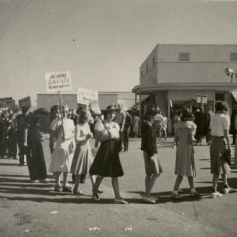 Line of women protesting, with a police officer visible in the background
