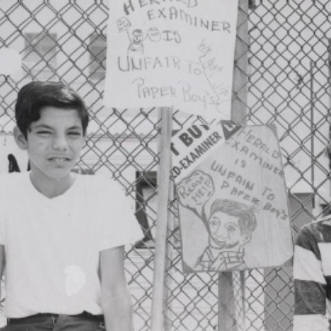 Two paper boys sitting in front of the "Berlin Wall" of the Herald-Examiner