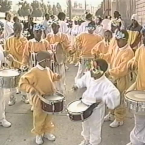 Children and young teens dressed in black and gold and masquerade masks play drums in unison. Harold Hambrick Collection.  Children and young teens dressed in black and gold and masquerade masks play drums in unison. Harold Hambrick Collection.