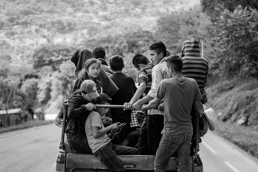 Many people riding in the back of a small pickup truck on a rural highway