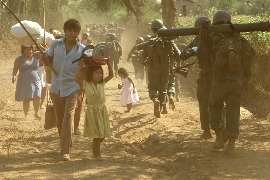 refugees and soldiers pass on a dirt road