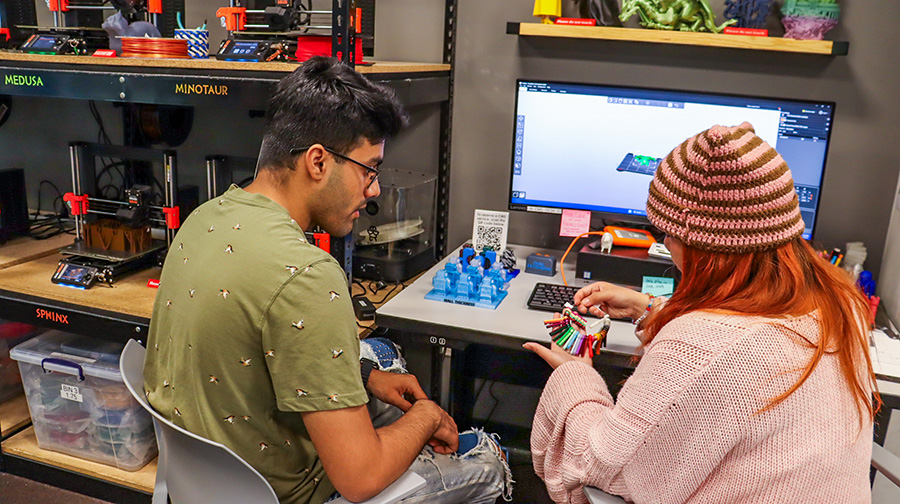 Two people inspecting some 3D model prints while sitting in front of a computer desk.