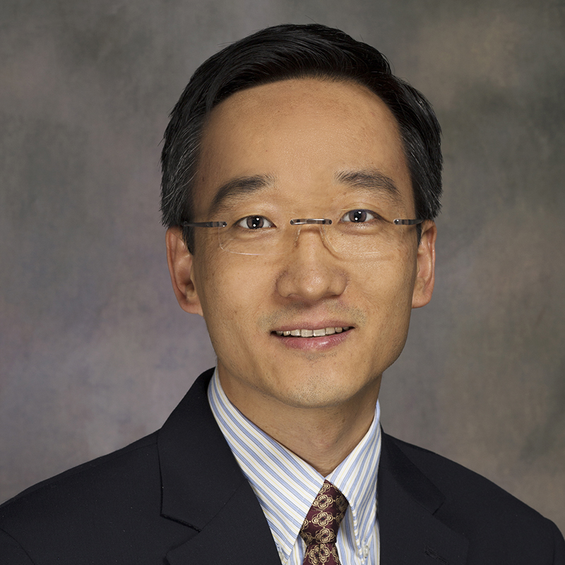 Profile of Shawn Sun wearing glasses and a suit amid a brownish background