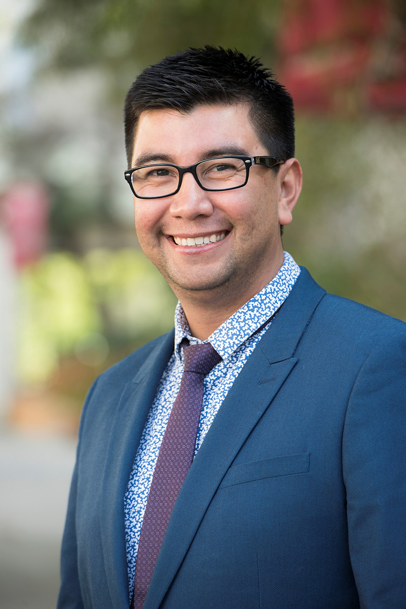 Proilfe of Stevie Ruiz wearing a blue suit and black glasses amid the outdoors