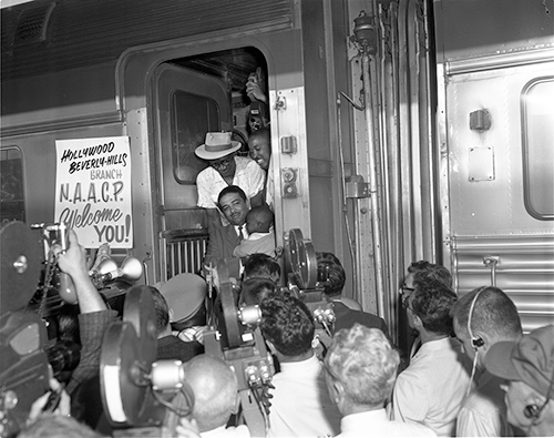 The Civil Rights activist Celes King III exits a train with a displaced Louisiana family arriving in LA, 1962. From Harry Adams Collection.