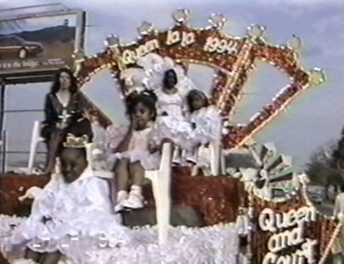 Children and the Queen of LALA 1994 dressed in white gowns sitting atop a red and gold float. From the Harold Hambrick Collection.