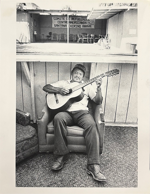 Middle-aged man playing guitar and a sign that says, “Comite De Refugiados Centroamericanos Santana Chirino Amaya  