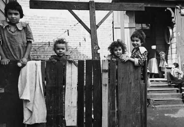 Four young children looking into the camera from behind a salvaged fence