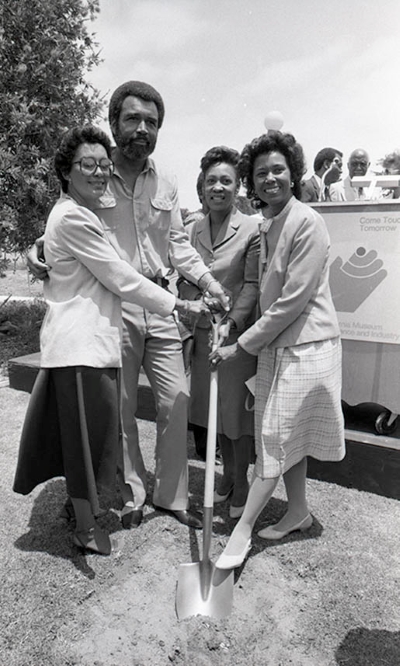 Yvonne Brathwaite Burke (right), Maxine Waters (2nd from right), and CAAM Director Aurelia Brooks pose while holding a shovel with an unidentified African American man during the groundbreaking ceremony for the California African American Museum in Los Angeles