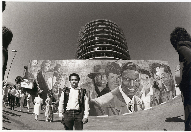 Artist Richard Wyatt, Jr with his mural Hollywood Jazz: 1945-1972 at the Capitol Records building, 1990, Roland Charles Collection
