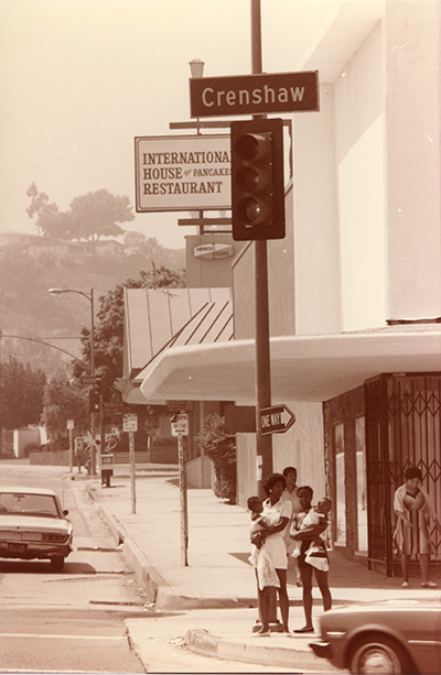 Residents wait for the traffic light as cars pass by on a Crenshaw corner, circa 1980-1989. Roland Charles Collection, Box 82