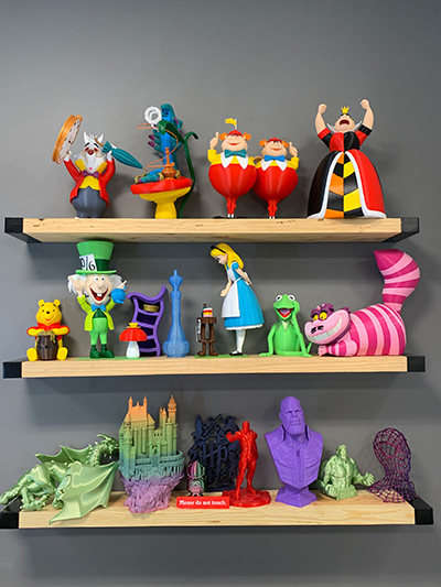 3 wall-mounted shelves with various colorful 3d printed object such as Winnie the Pooh, the Cheshire cat, and Thanos