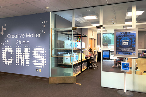 View through the door of the Creative Maker Studio showing 3d printers and a student using a computer