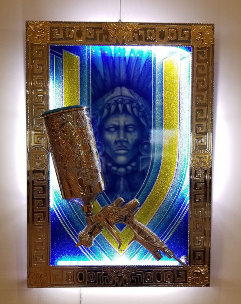 gold colored frame with etchings and a gilded and etched airbrush with an indigenous figure airbrushed on a representation of a car hood