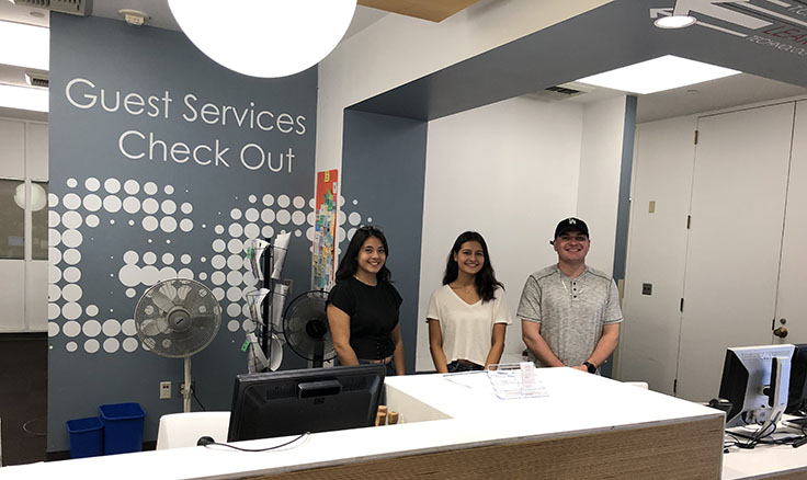 Three students standing behind a service desk
