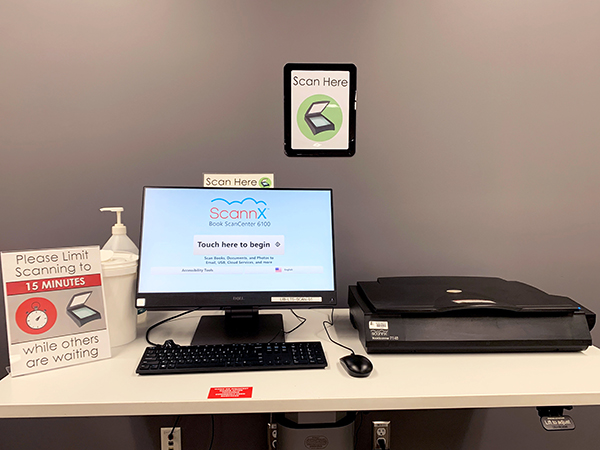 A table with a scanner next to a keyboard and monitor with a sign saying "Scan Here"