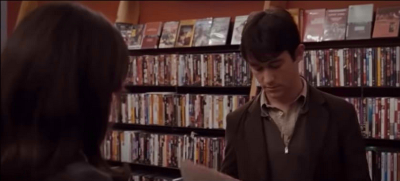 A man looking at a disc vynil record at a bookstore while a woman is facing him with the back of her head in the foreground.