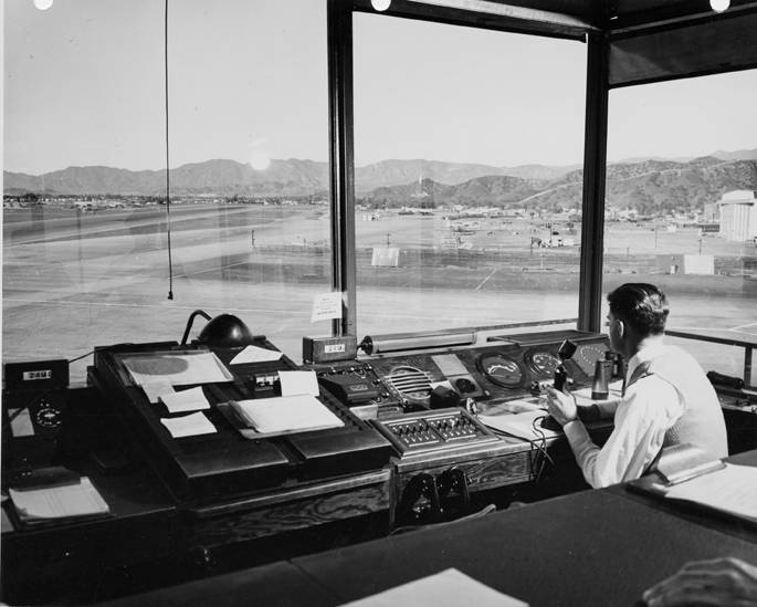 Interior view of an air traffic controller sitting in front of a microphone in the controller tower