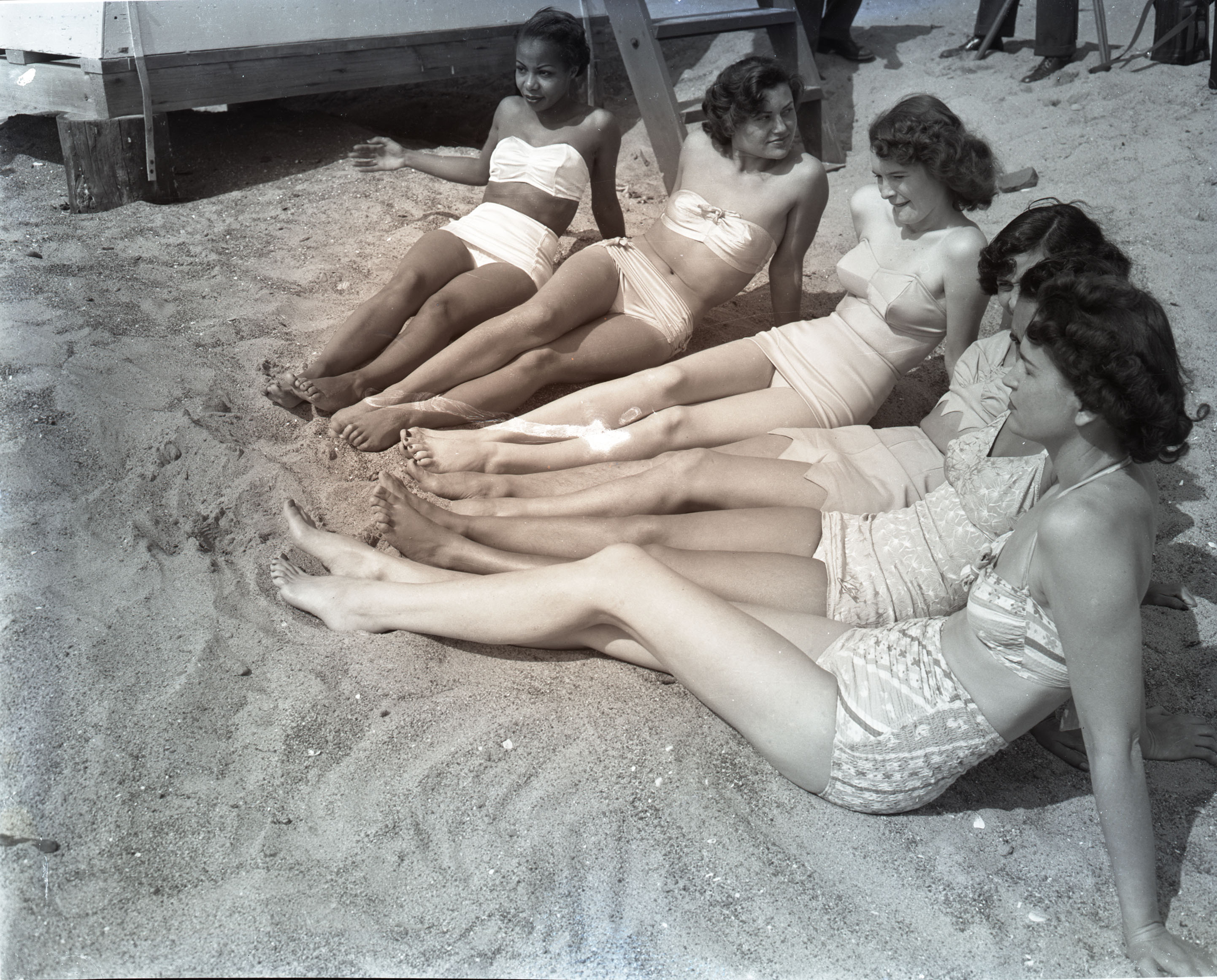 6 women in swimsuits sitting together on the sand