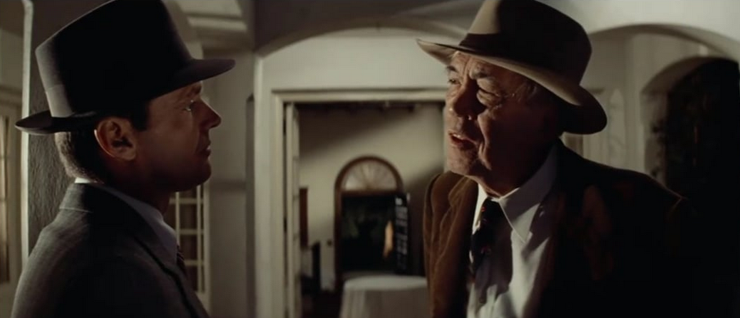 Two men in suits and hats talking with each other