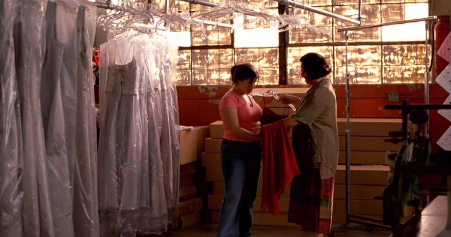 Two women discussing while looking at a dress that one of them is holding; Other garments are inside plastic covers and hanging from rods next to them.